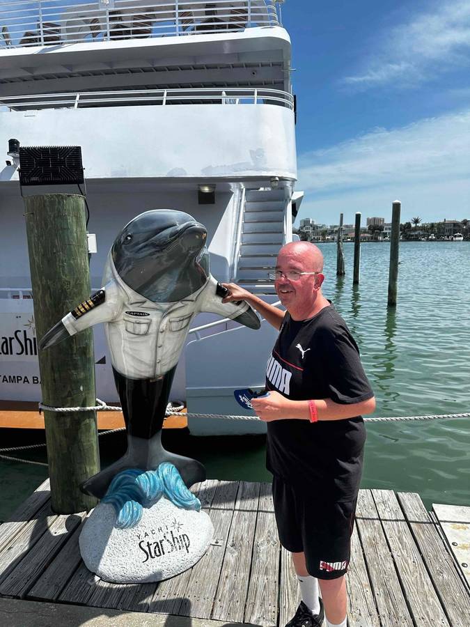 A community member posing with a dolphin statue by the water